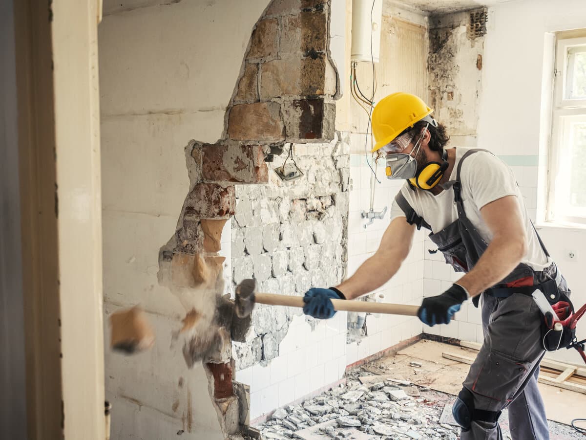 A worker in a respirator and hard hat stripping material from a wall during an abatement job