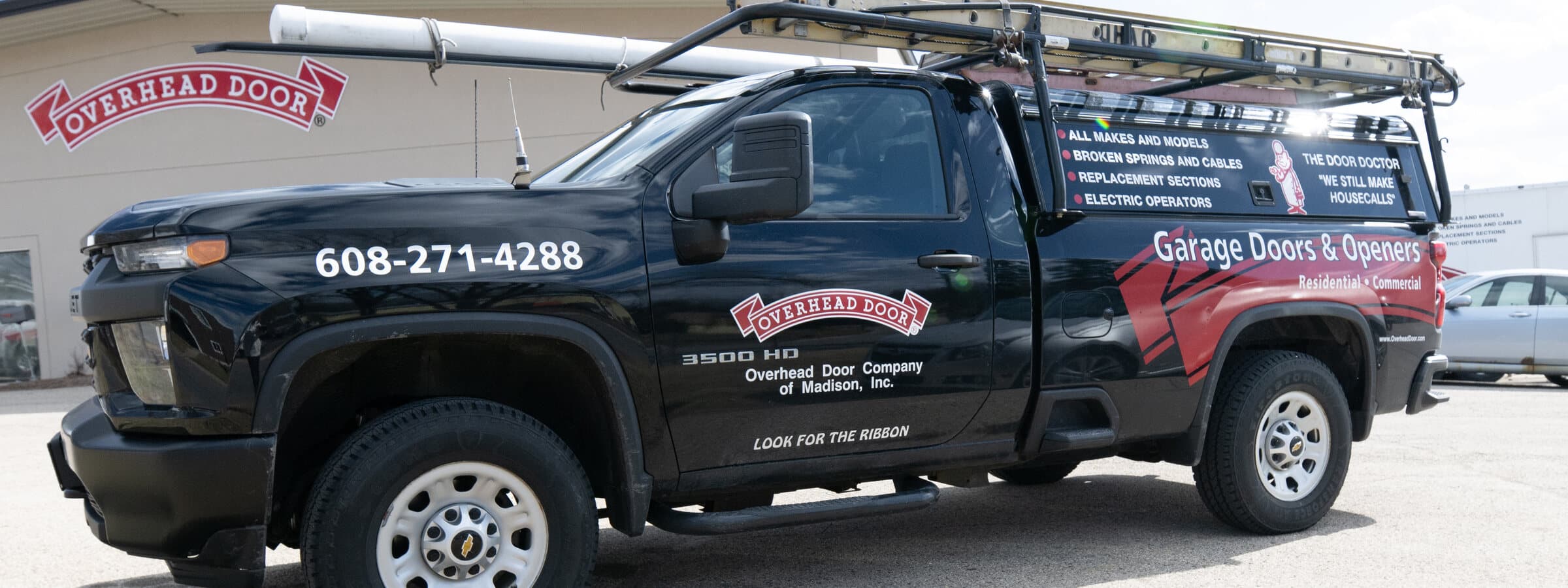 A garage-door company's branded service truck, ladder rack loaded, parked outside its shop