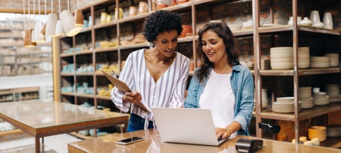 Two women collaborating over laptop in pottery shop