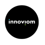 A black circle with the word "innoviom" in lowercase white letters at the center. The i's are dotted with a blue dot above the first "i" and a green dot above the second "i". This logo reflects its roots as an innovative marketing agency based in Madison, WI.