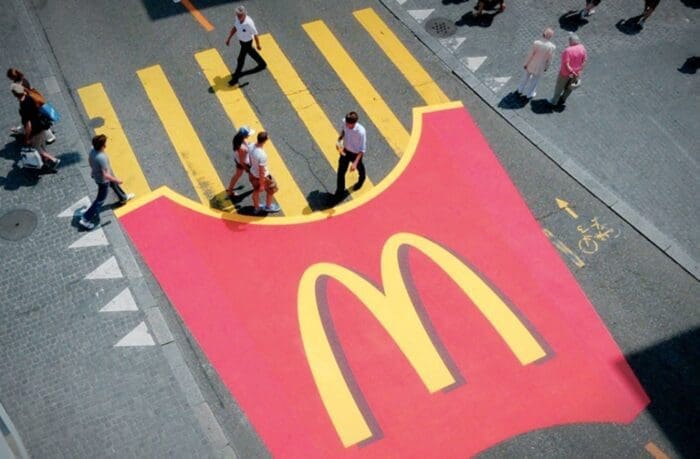 Pedestrians crossing over large McDonald's logo on street