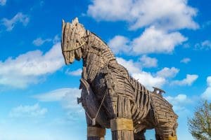 A large wooden sculpture resembling the Trojan Horse stands against a bright blue sky with scattered white clouds. The intricate design features wooden planks and beams tied together with ropes, creating a striking ancient and mythical appearance—like a landmark for asymmetric marketing strategy in Madison, WI.