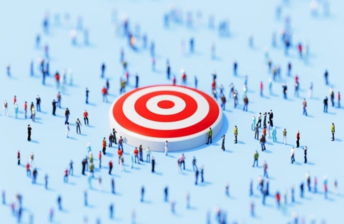 Miniature people gathering around large target on blue