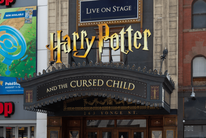 A theater marquee displays the title "Harry Potter and the Cursed Child" at 263 Yonge St. The sign is ornately designed with gold lettering and decorative elements. Above, a sign reads "Live on Stage." Fortune favors the prepared as visitors explore adjacent buildings and storefronts.