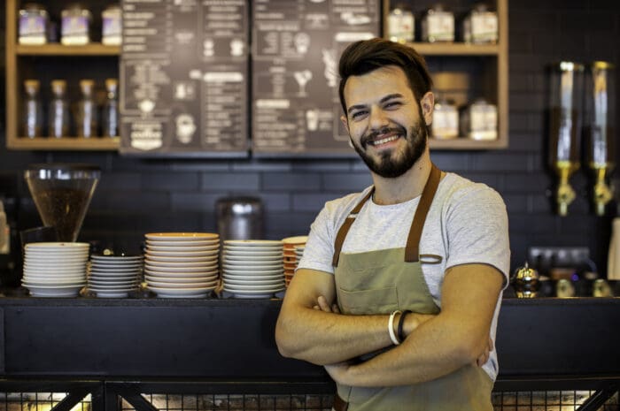 Barista smiling in front of a coffee shop counter.