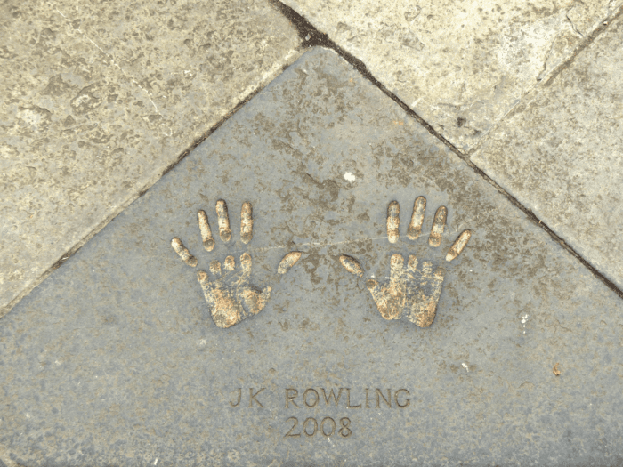 A pair of handprints embedded in a gray paving stone with the inscription "JK ROWLING 2008" engraved beneath them. The handprints, slightly worn and surrounded by square tiles, serve as a testament to the idea that fortune favors the prepared.