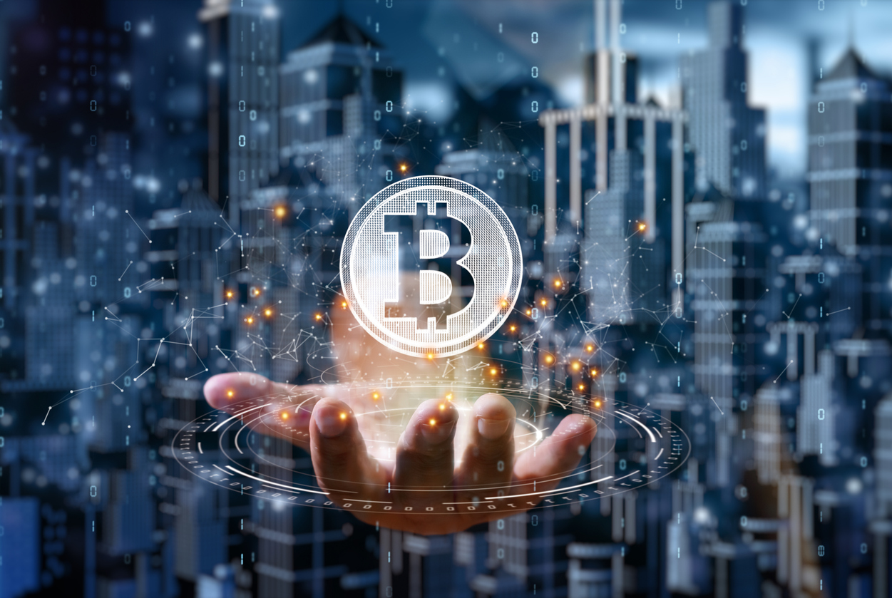 Hand displaying holographic Bitcoin over cityscape