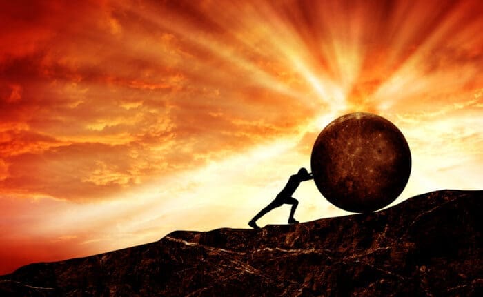 Silhouette of a person pushing a large spherical boulder up a steep, rocky slope. The background features an intense, vibrant sky with rays of sunlight breaking through fiery red and orange clouds, creating a dramatic, almost surreal atmosphere. Diligence is the mother of good luck in this struggle.