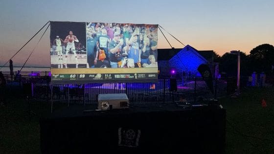 Outdoor evening event with large screen displaying sports game