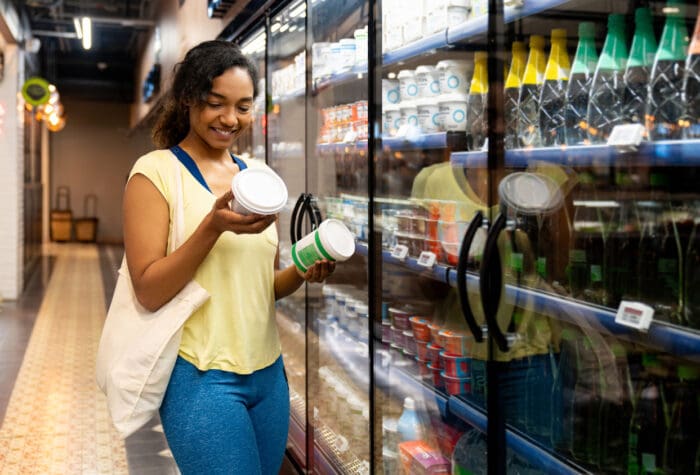 Woman comparing yogurt brands in grocery store aisle as an example of price competitor.