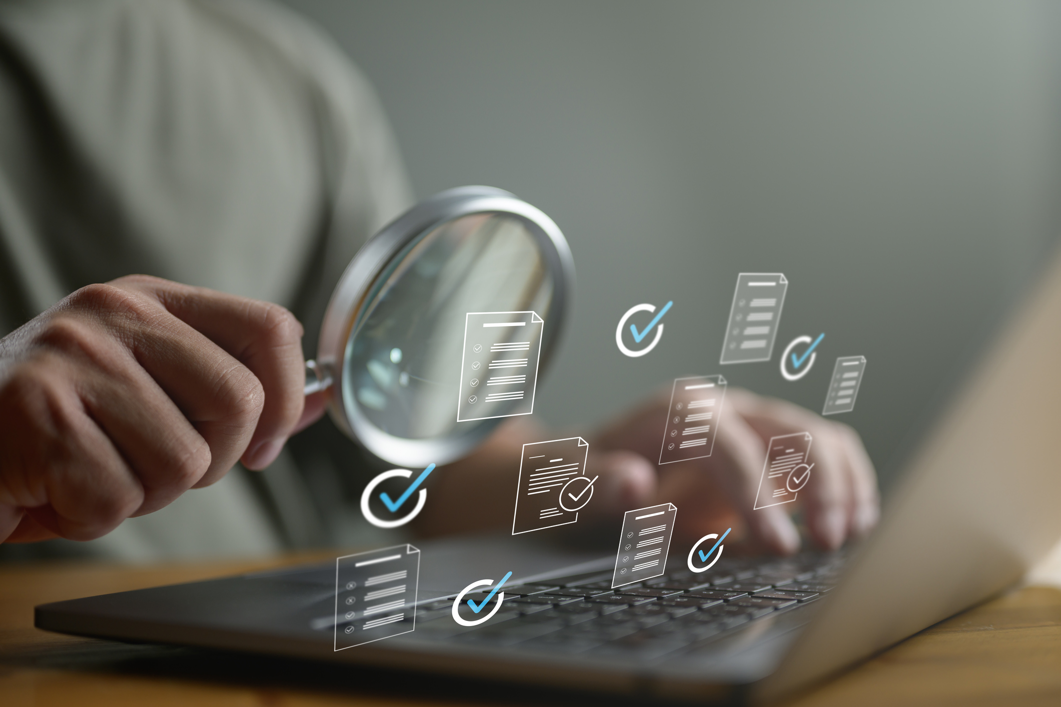 A person holds a magnifying glass over a laptop keyboard while floating digital icons of documents with checkmarks are visible, suggesting document review or verification. This scene reflects the meticulous nature of a competitive audit.