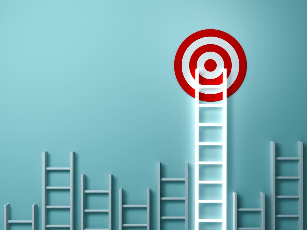 A series of ladders of varying heights leans against a blue wall. One prominent ladder reaches a red and white target symbol, suggesting the concept of achieving a goal through competitive benchmarking.