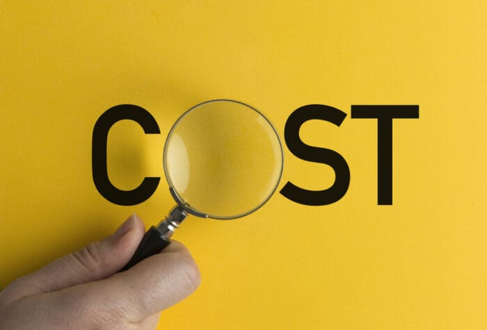 Magnifying glass over word 'cost' on yellow background.