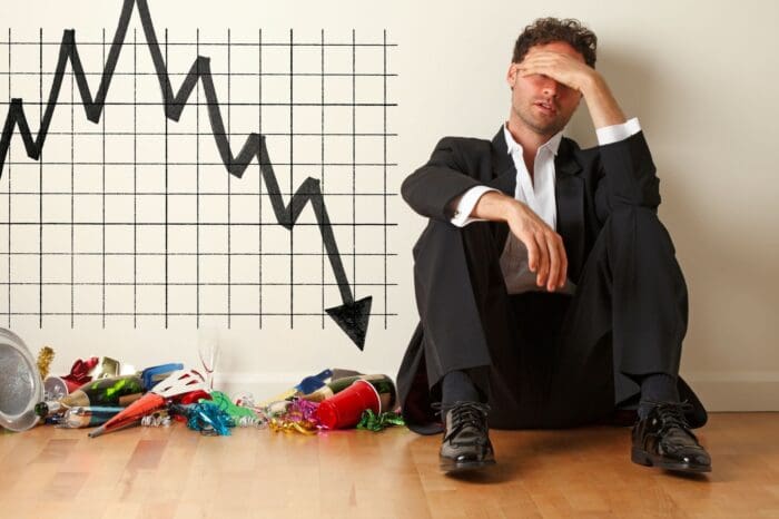 Stressed man beside declining financial chart and clutter.