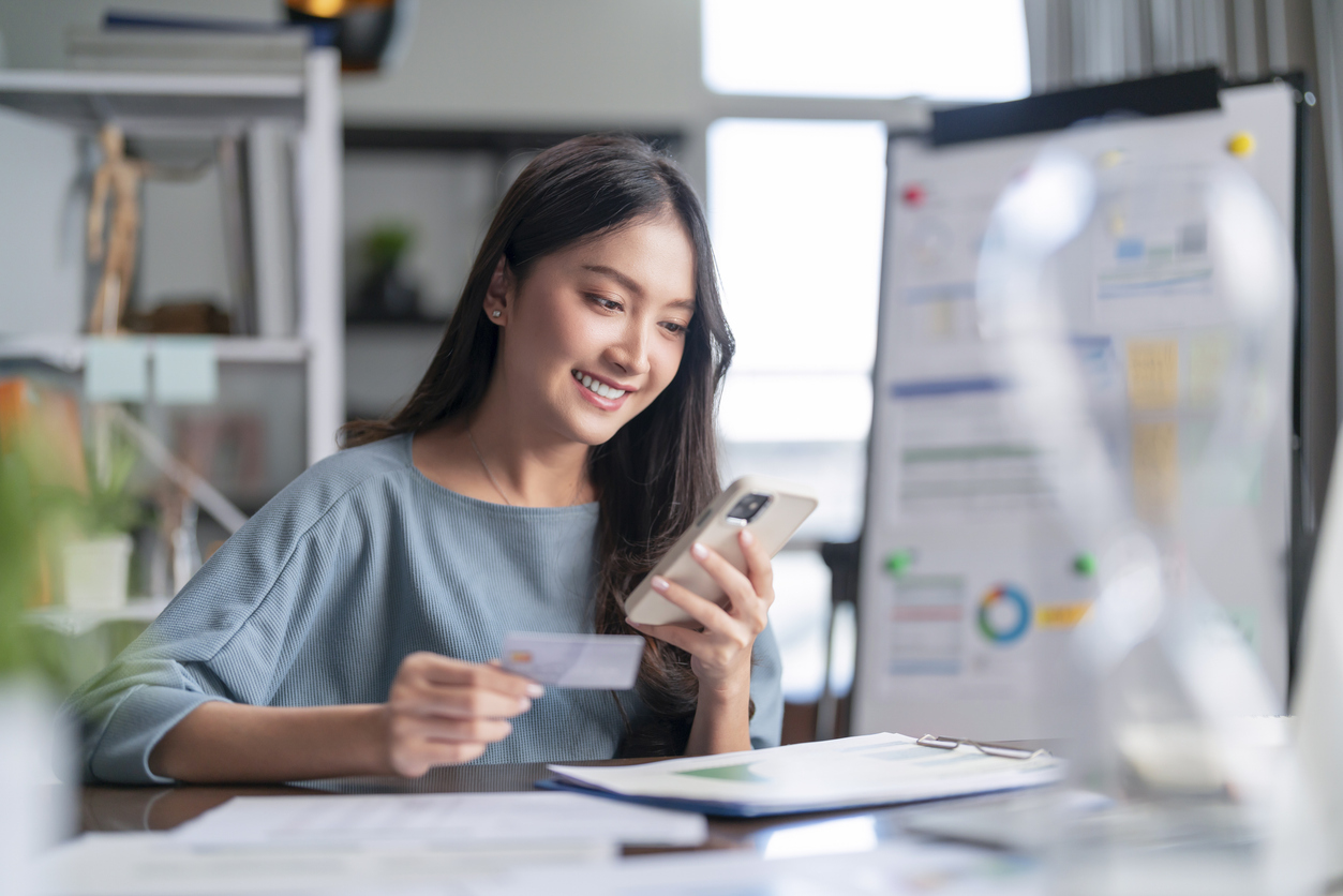Woman smiling using smartphone and holding credit card